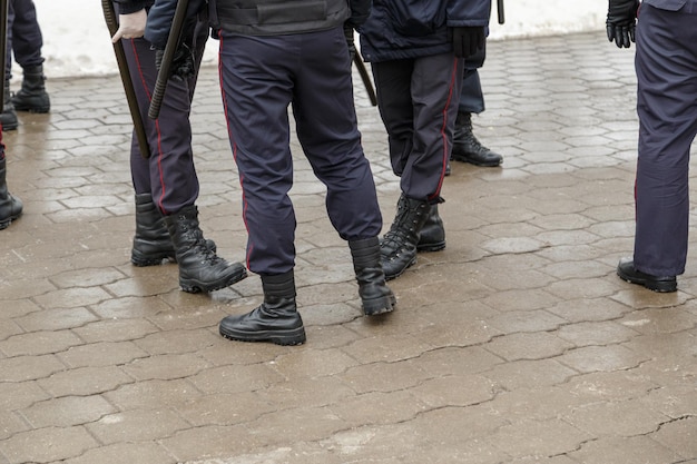 Gambe degli ufficiali di polizia russi in stivaletti neri pantaloni a strisce rosse e con bastoncini notturni in gomma tonfa sulla superficie del pavimento bagnato con messa a fuoco selettiva e sfocatura