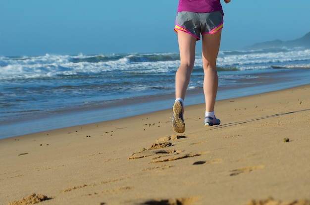 Gambe del corridore della donna in scarpe sul concetto della spiaggia, di funzionamento e di sport