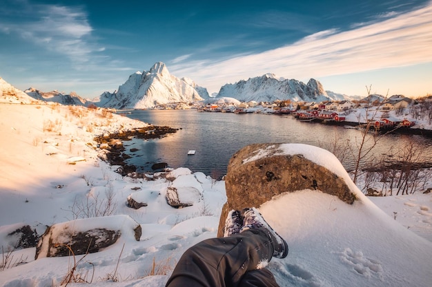 Gambe del viaggiatore che si rilassano nella città innevata di Reine sulla linea costiera alle isole di Lofoten, Norvegia