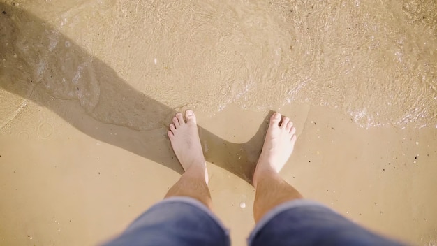 Gambe dell'uomo caucasico abbronzato sulla spiaggia sabbiosa al mare