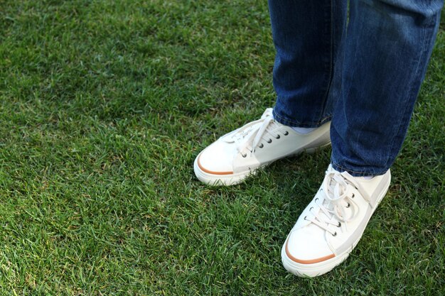 Gambe dell'uomo in jeans e scarpe da ginnastica bianche sul prato.