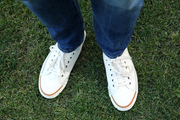 Gambe dell'uomo in jeans e scarpe da ginnastica bianche sul prato.