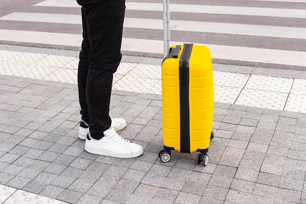 gambe dell'uomo in jeans neri e scarpe da ginnastica bianche con valigia gialla Concetto di viaggio d'affari