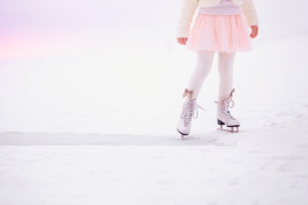 Gambe della bambina che pattina sul ghiaccio nella luce del mattino all'alba.