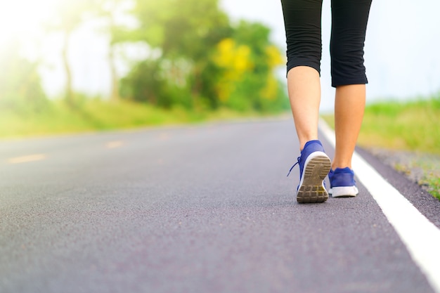 Gambe della donna che camminano nel parco, corridore femminile che funziona sulla strada fuori