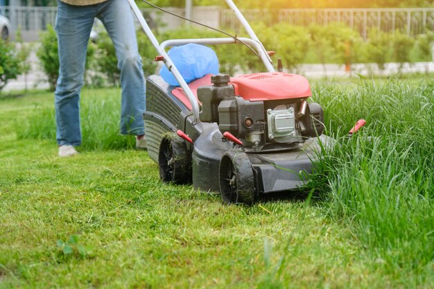 Gambe della donna del giardiniere che falciano erba con la falciatrice