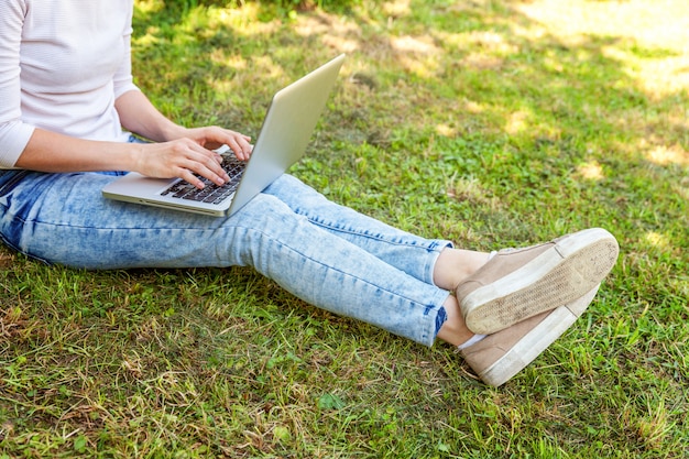 Gambe della donna sul prato inglese dell&#39;erba verde nel parco della città, mani che lavorano al computer portatile