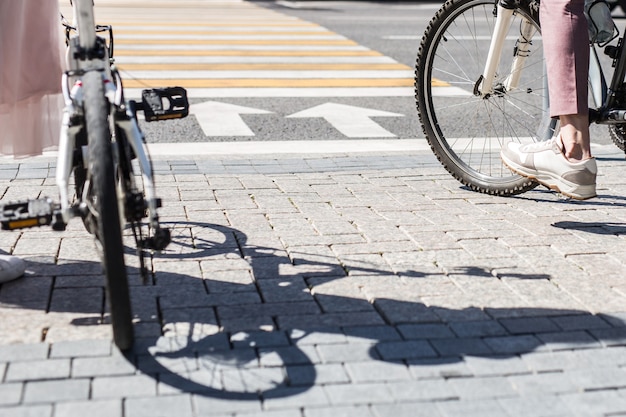 Gambe di donna in piedi vicino a bicicletta e gambe di uomo in bicicletta sulla piastrella del marciapiede di fronte all'incrocio