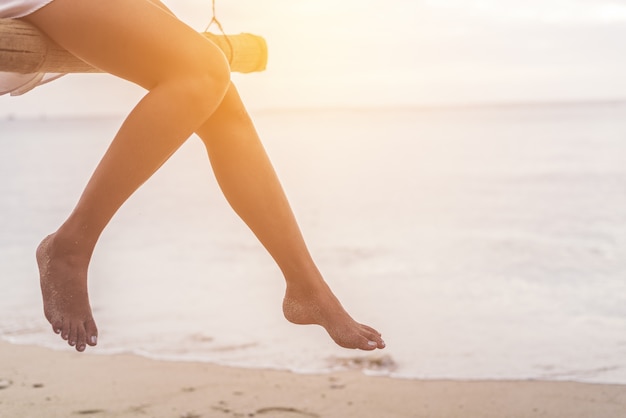 Gambe di donna in spiaggia su altalena in legno