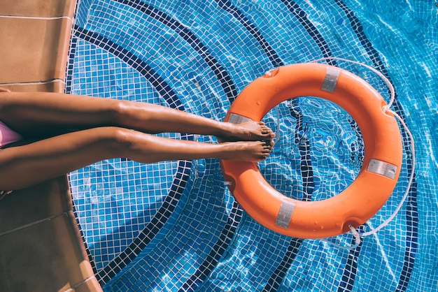 Gambe di donna in una piscina con salvagente