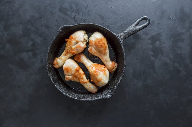 Gambe di pollo fritto su una tavola nera in una vecchia pentola.