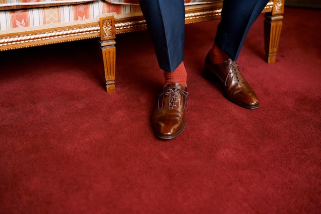 Gambe di un uomo in pantaloni blu calzini rossi e scarpe marroni seduto su un divano in primo piano camera d'albergo