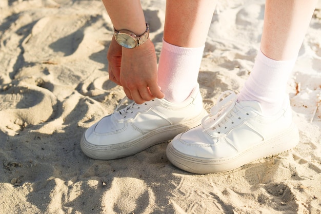 Gambe di una ragazza con una gonna in scarpe da ginnastica alla moda sulla sabbia l'immagine viene portata a fare una passeggiata