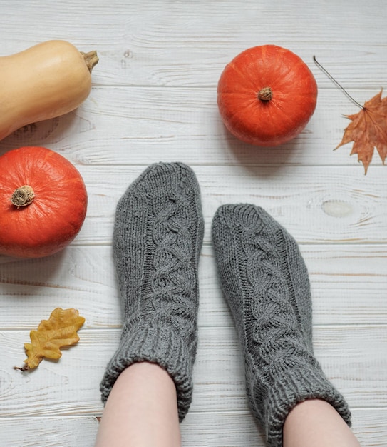 Gambe di una ragazza in calzini lavorati a maglia su uno sfondo di legno accanto a zucche e foglie d'autunno
