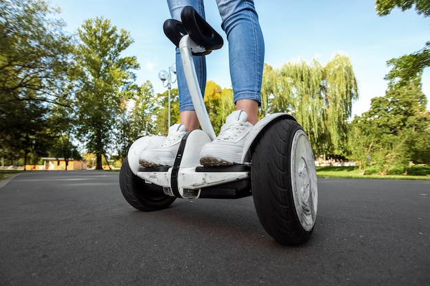 Gambe di una ragazza in scarpe da tennis bianche su un hoverboard bianco in un primo piano del parco