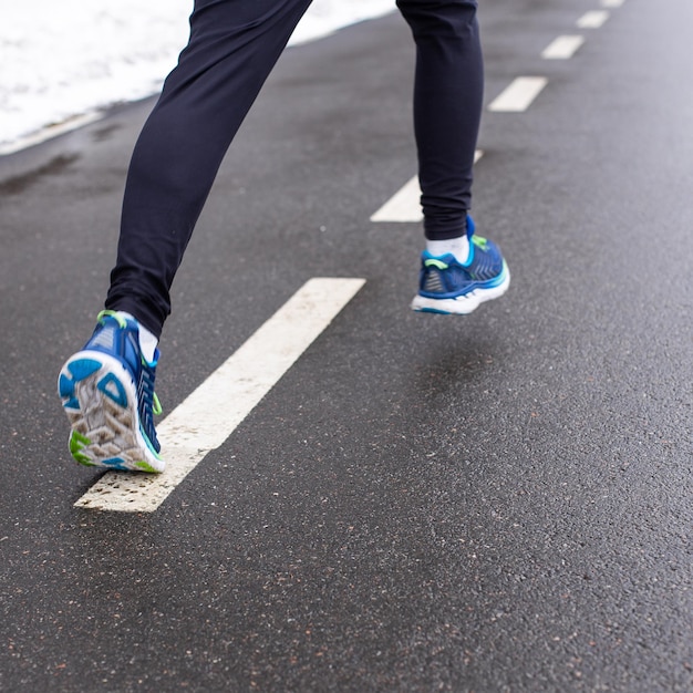 Gambe di uomo che corre in scarpe e pantaloni sportivi. Corridore sulla pista stradale.