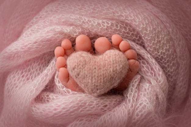 Gambe, dita dei piedi, piedi e talloni di un neonato. Avvolto in una coperta a maglia grigia, beige, rosa, bianca. Cuore lavorato a maglia nelle gambe del bambino. Foto in bianco e nero. Foto di alta qualità