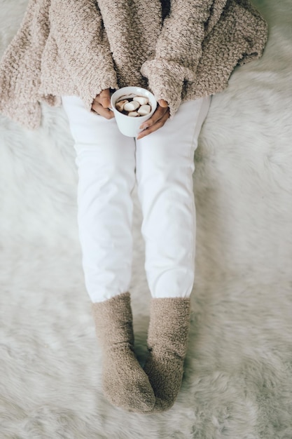 Gambe donna in calzini caldi su coperta di pelliccia morbida con tazza di cioccolato Accoglienti momenti di relax a casa