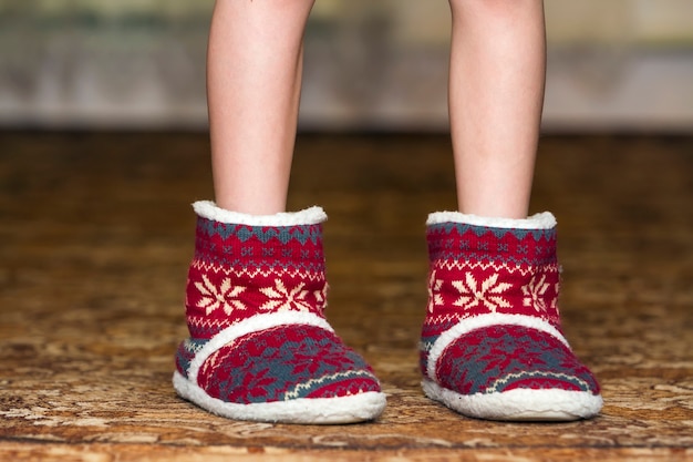 Gambe e piedi nudi del bambino in stivali rossi di natale di inverno con il modello dell'ornamento