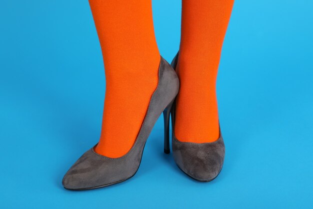 Gambe femminili in calzini arancioni e tacchi su sfondo blu