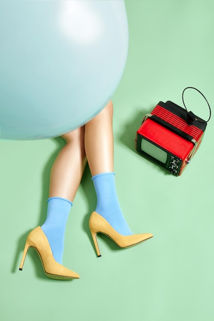 Gambe femminili in calzini e scarpe col tacco alto su sfondo studio con tv vintage