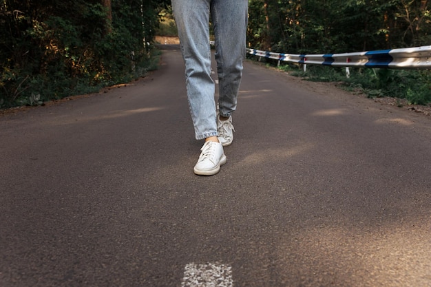 Gambe femminili in scarpe da ginnastica bianche e jeans