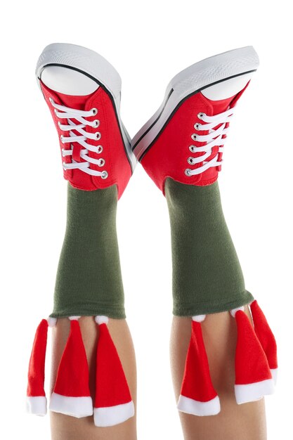 Gambe femminili in scarpe da ginnastica rosse e calze verdi con cappelli di Babbo Natale isolati su sfondo bianco