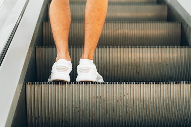 Gambe in piedi sulla scala mobile di un centro commerciale