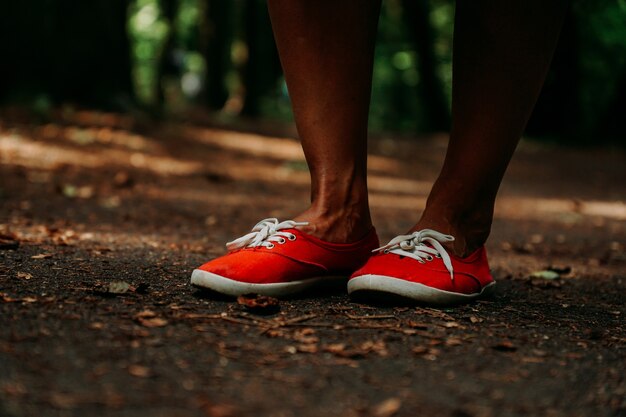 Gambe in scarpe da ginnastica rosse su un percorso autunnale nel parco. Gambe in pelle nera. Sport nella foresta d'estate