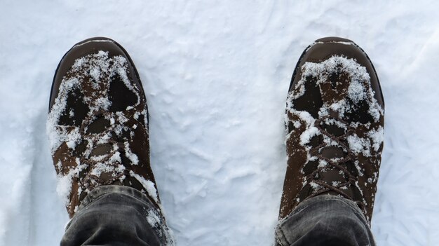 Gambe maschili in stivali invernali coperti di neve, vista dall'alto. Passeggiata invernale nella neve. Concentrati sulle gambe. Bel tempo invernale bianco con nevicate fresche.