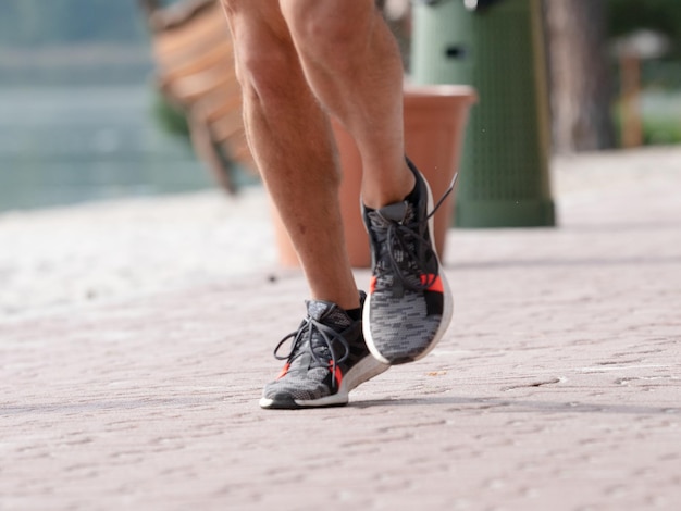 Gambe maschili nude in scarpe da ginnastica da corsa in corsa su marciapiede rosso nel parco della città