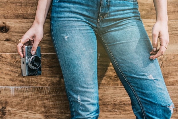 Gambe ritagliate dei jeans della donna con la vecchia macchina fotografica d'annata