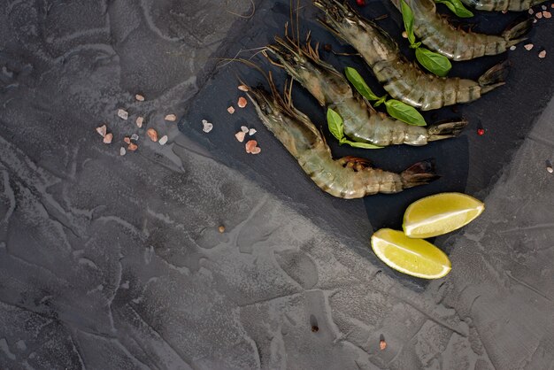 Gamberetti crudi freschi con calce e spezie su una tavola di pietra. I frutti di mare sani sono una fonte di proteine. Disteso. Copia spazio.