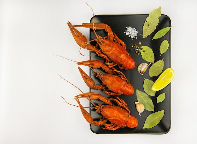 Gamberi bolliti con limone, erbe aromatiche e aglio su un piatto nero su sfondo bianco. Copia spazio.