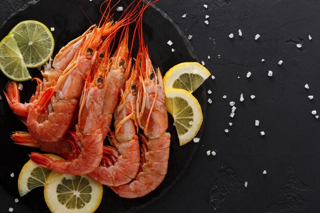 Gamberi bolliti con limone su sfondo nero, copia dello spazio. Vista dall'alto su appetitosi snack a base di pesce, servizio ristorante.