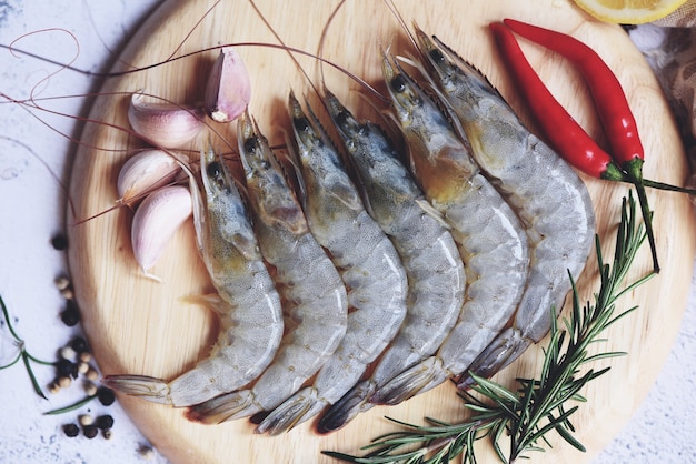 Gamberi crudi su piatto bianco, frutti di mare freschi di gamberetti con erbe e spezie per cibi cotti