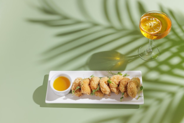 Gamberi fritti con un cocktail su uno sfondo verde chiaro con un'ombra da una vista dall'alto di una palma