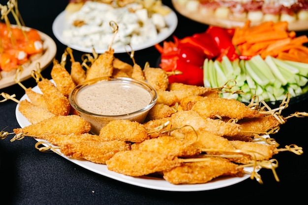 Gamberi fritti impanati su spiedini con salsa di noci su un piatto tra antipasti e bastoncini di verdure