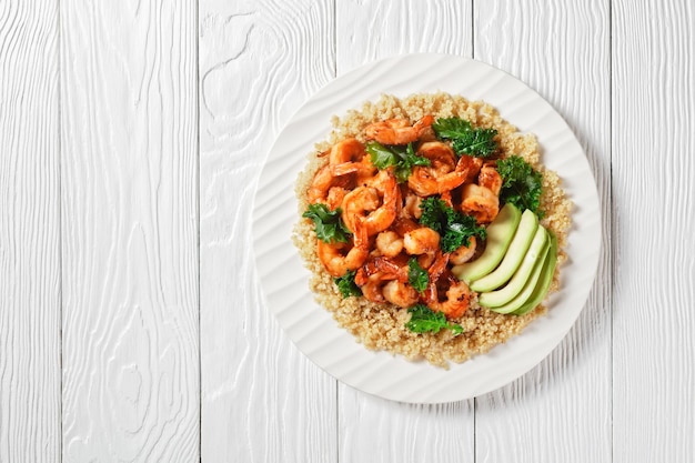 Gamberi piccanti alla griglia serviti con cavolo nero di quinoa e avocado su un piatto bianco piatto e spazio libero