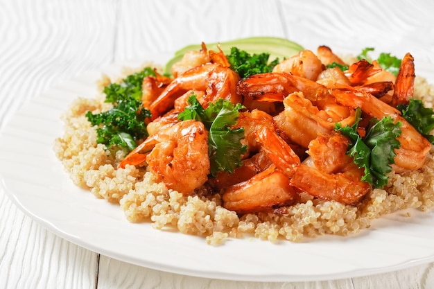 gamberi piccanti alla griglia serviti con quinoa, cavolo nero e avocado su un piatto bianco