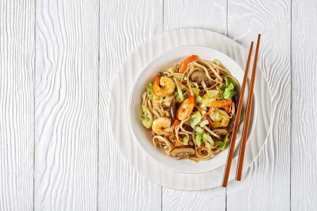 Gamberi Yaki Udon Tagliatelle udon saltate in padella con gamberetti Cavolo Funghi di castagne Cipollotto carota mirin e salsa di soia in una ciotola bianca con le bacchette piatte spazio libero cucina giapponese