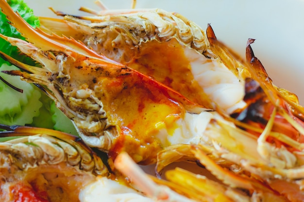 Gamberoni di fiume alla griglia con salsa di frutti di mare piccante in disco bianco.