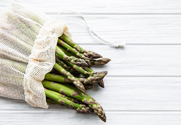 Gambi di asparagi in un sacchetto a rete ecologica su un vecchio fondo di legno