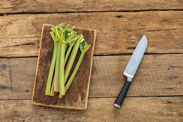 Gambi di rabarbaro e coltello da cucina sulla vista del vecchio tavolo in legno