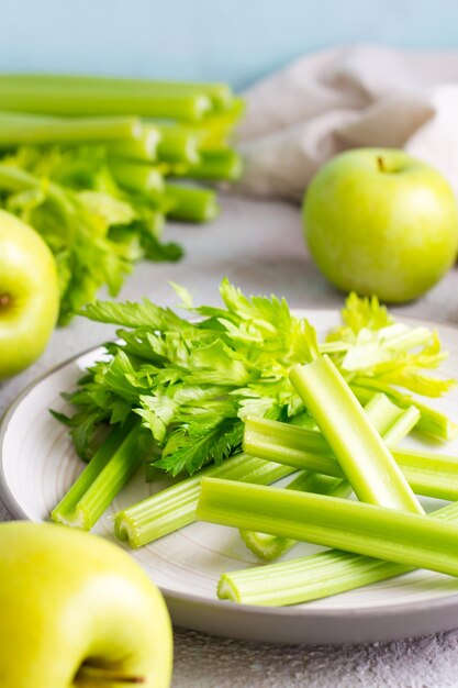 Gambo di sedano fresco affettato con foglie su un piatto e mele verdi sul tavolo pronte per essere cucinate. Cibo vegetariano. Vista verticale. Avvicinamento