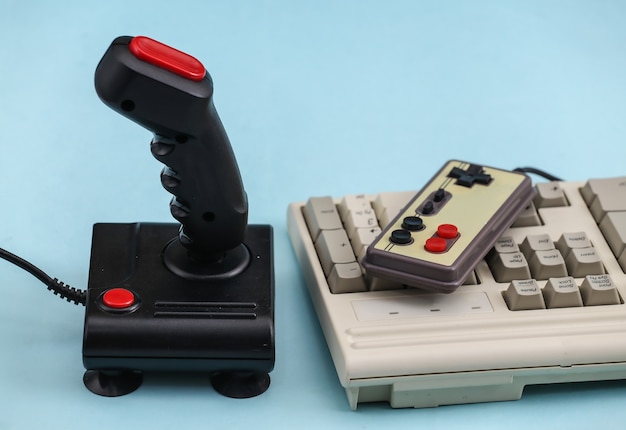 Gamepad retrò e joystick con tastiera pc su sfondo blu. Videogioco, giochi anni '80.