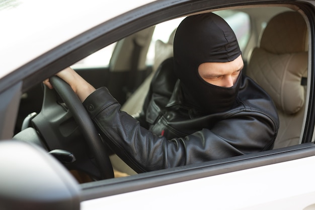 gangster in una maschera nera ruba la macchina di qualcun altro