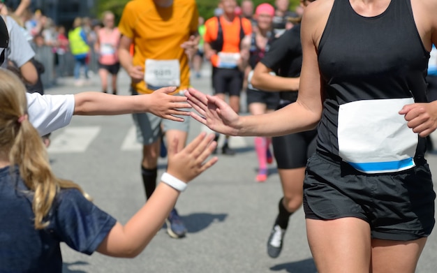 Gara podistica maratona, supporto corridori su gara su strada, mano del bambino che dà il cinque, atleti che supportano il bambino che corre, concetto di sport