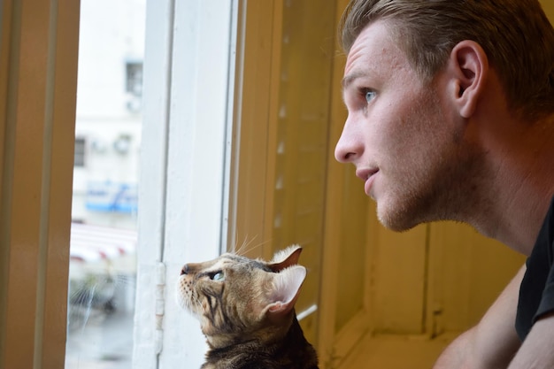 Gatto e uomo che guardano attraverso la finestra