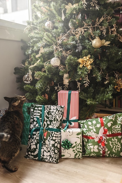 Gatto oltre a una pila di regali sotto un albero di Natale decorato